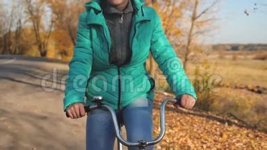 小女孩正在秋天的公园里骑自行车上路。 女孩的手拿着自行车的弯轮。 体育运动